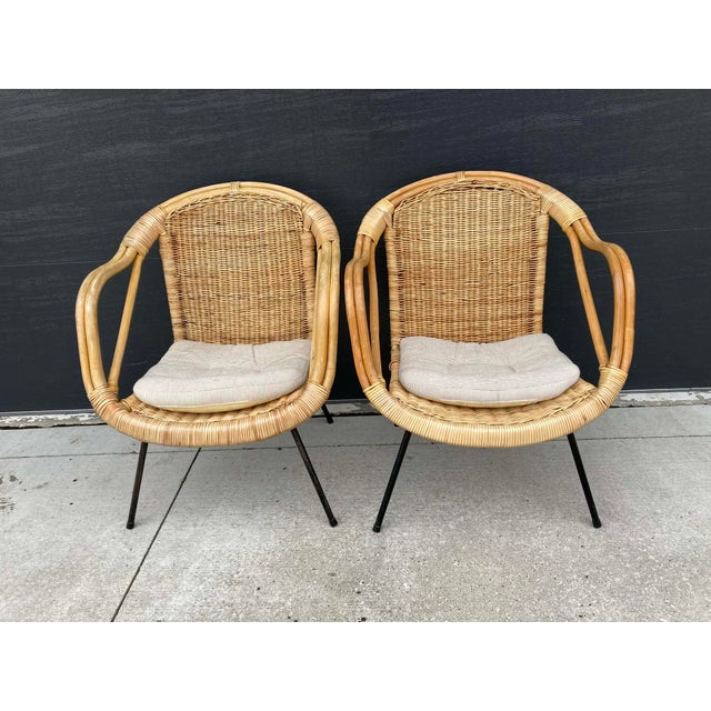 The chairs feature handwoven rattan seats and backs, framed by curved wooden arms and supported by sleek black metal legs,...