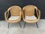 The chairs feature handwoven rattan seats and backs, framed by curved wooden arms and supported by sleek black metal legs,...