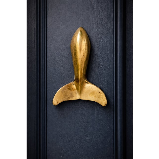 This whimsical door knocker will make everyone who comes to your door smile. The solid brass whale fin shape has a knocker...