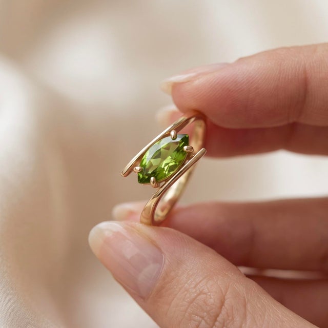 Infuse vibrant color into your look with this eye-catching bypass ring starring a lively marquise-cut Peridot. The...