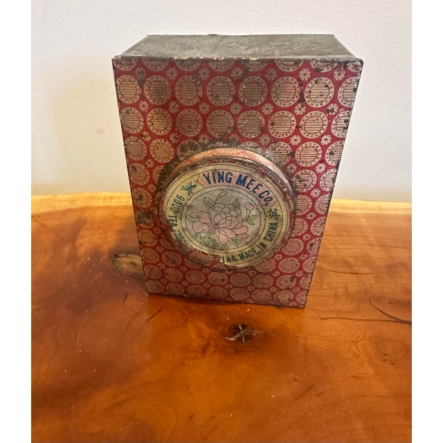 A beautifully aged rectangular tin box featuring a patterned red lid with a raised floral medallion centerpiece. The...