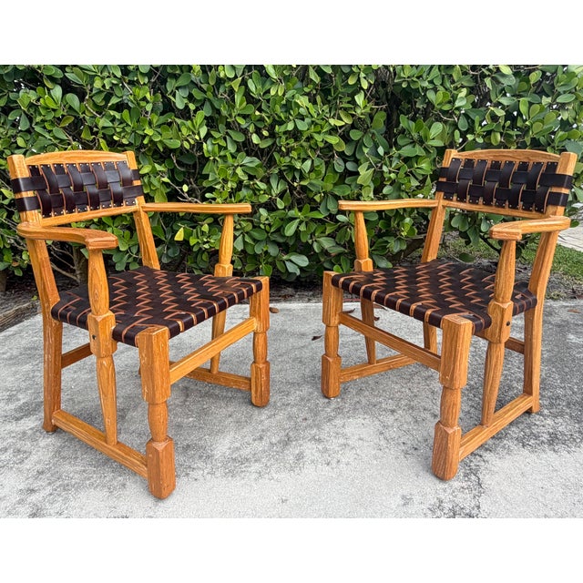 A handsome pair of vintage mid-century Ranch Oak arm chairs featuring solid oak frames with woven leather strap backs and...