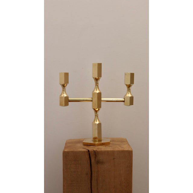 Made in Sweden. This exquisite three-arm candelabra, crafted from solid brass, is a design masterpiece produced by Gusum...