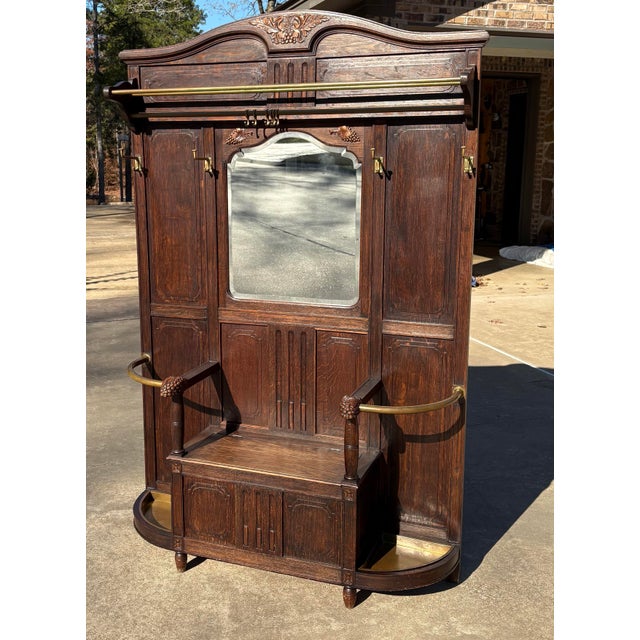 Gorgeous antique hall tree with a built in bench seat with storage under. Brass drip trays and curved bars at the base are...