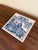 A classic Dutch Delft-style hand painted blue and white porcelain tile featuring a scene of women pharmacists in rich...