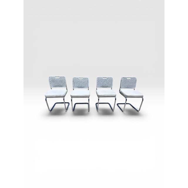 A stylish set of four vintage cantilever dining chairs featuring polished tubular chrome frames, woven white rattan-style...
