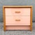 A refined postmodern nightstand that blends soft color with warm natural elements. Finished in a blush pink high-gloss...