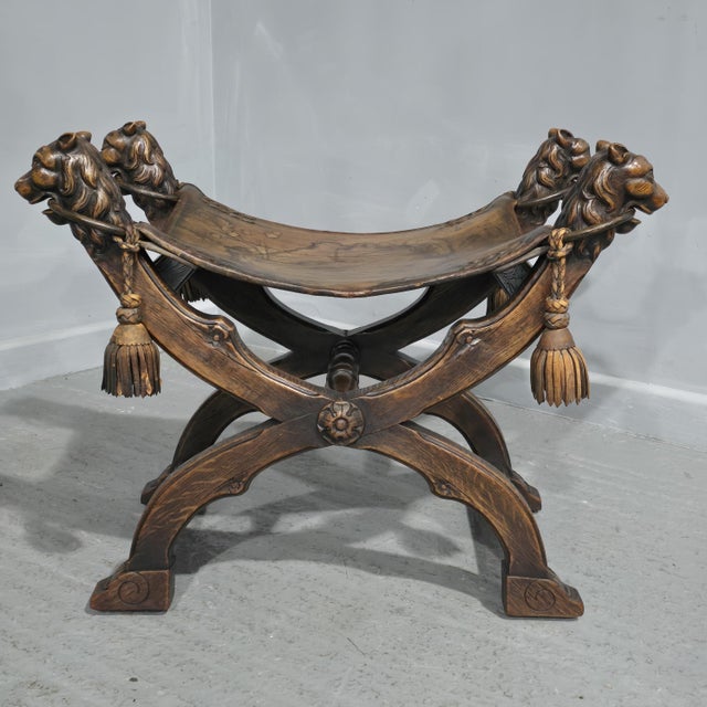 An outstanding Walnut X framed stool with a leather seat, carved lion heads holding steel rings with leather straps, lion...