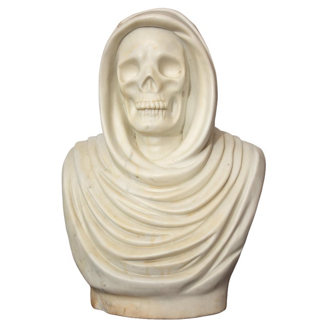 A finely carved solid marble bust depicting a hooded skeletal figure, this striking memento mori sculpture presents a...