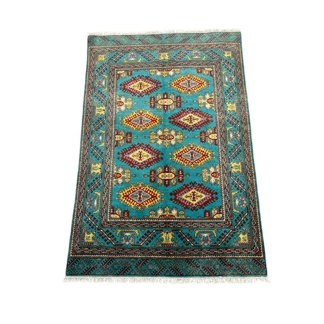 This naturally dyed wool Kazak rug has a vivid turquoise field filled with repeating medallions in burgundy, golden...
