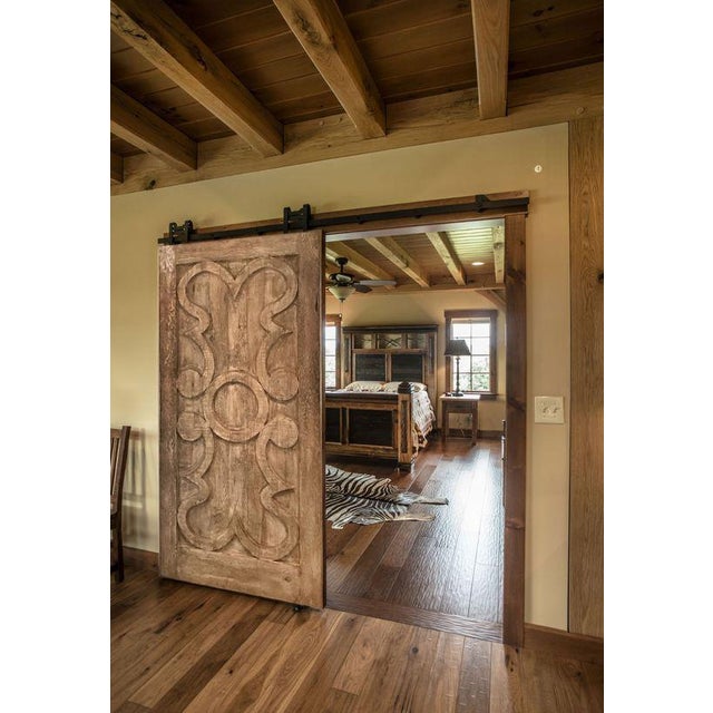 This handcrafted solid wood barn door features an elegant carved Classical Scroll Pattern with soft, flowing geometry —...