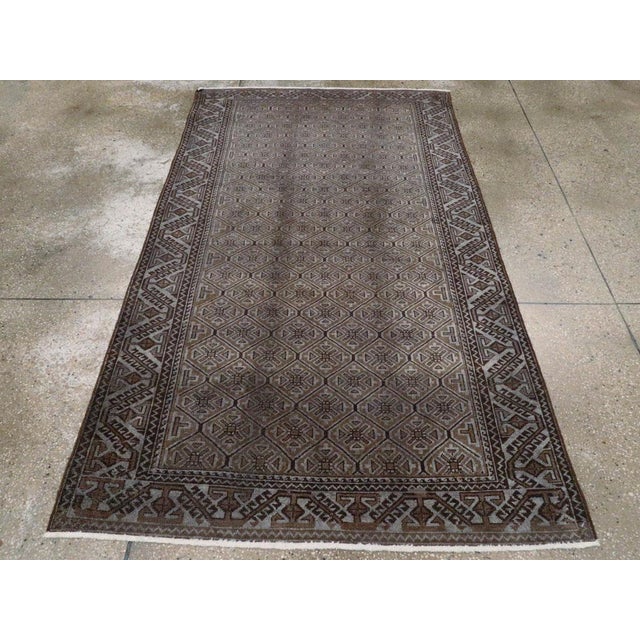 This early 20th-century Persian Baluch rug presents a tightly organized allover geometric composition in warm brown,...