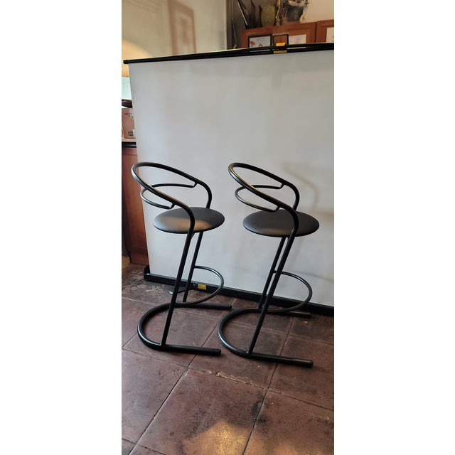 A very stylish 1980s Art Deco Modern Modernist style pair of bar stools. Made of black metal and Faux leather seat.