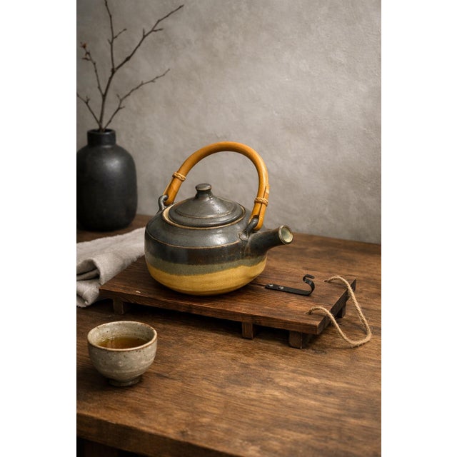 Signed “Walker 1979,” this handcrafted studio pottery teapot features a rich earth-tone glaze, bamboo-wrapped handle, and...