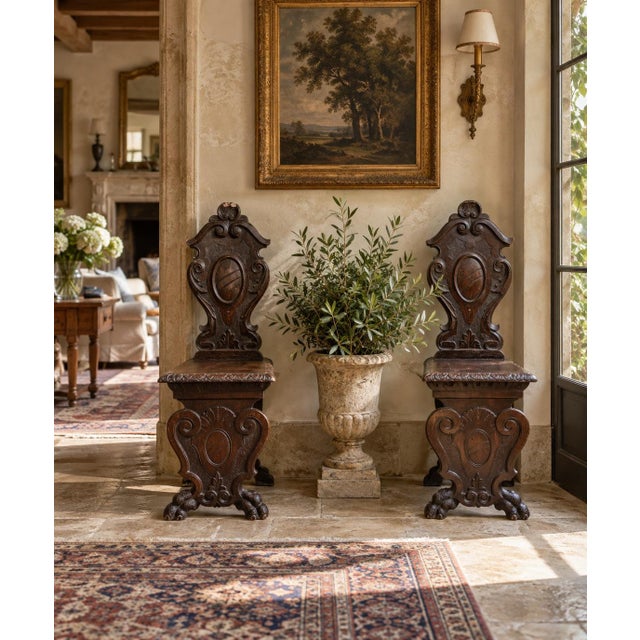 A striking pair of antique Italian Renaissance Revival hall chairs crafted from richly toned walnut and adorned with...