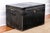 An antique black leather trunk edged with decorative brass studs, iron handles and iron lock plate and hasp with keyhole....