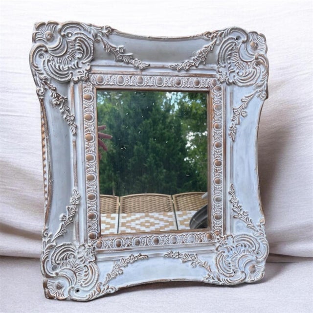 This French Country wall mirror features a heavily distressed white frame with gold trim. Ornate wooden with cutouts details.