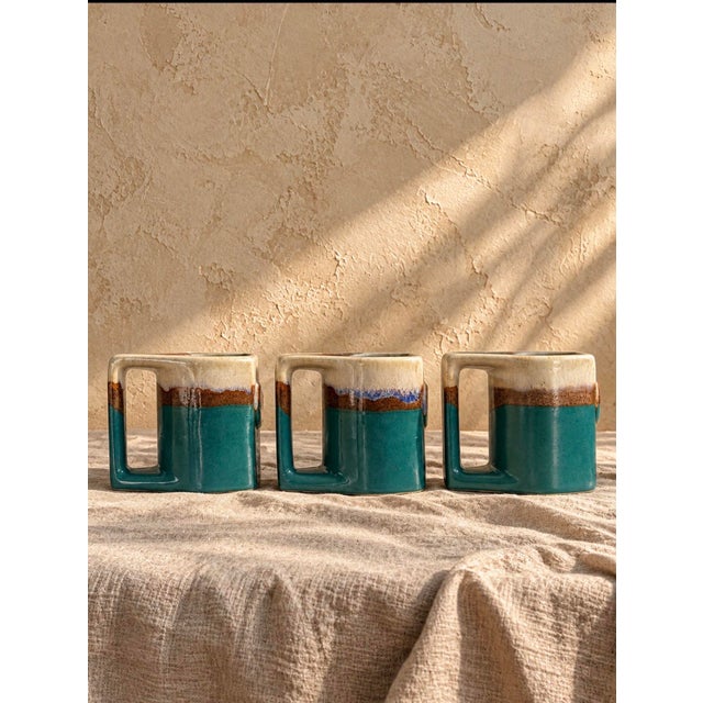 Charming set of three vintage 1980s Padilla ceramic mugs featuring a rich teal glaze, creamy neutral upper sections, and...