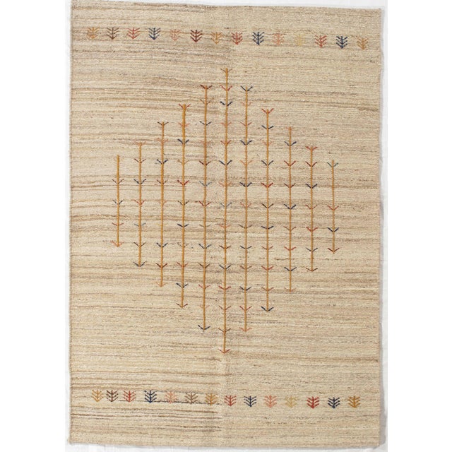 Hand-knotted Sumak rug featuring a soft beige field with a central diamond-shaped arrangement of stylized tree motifs. The...