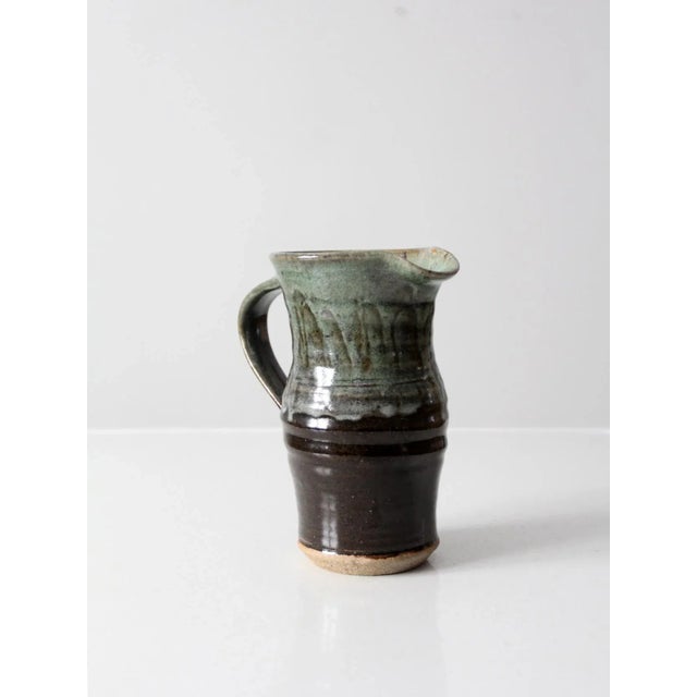 This is a vintage studio pottery pitcher in hand-thrown ceramic with a rich brown and green glaze. organic form with...