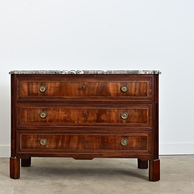 A substantial French commode from the 19th century wrapped in finely-grained mahogany trimmed with inlaid brass that...