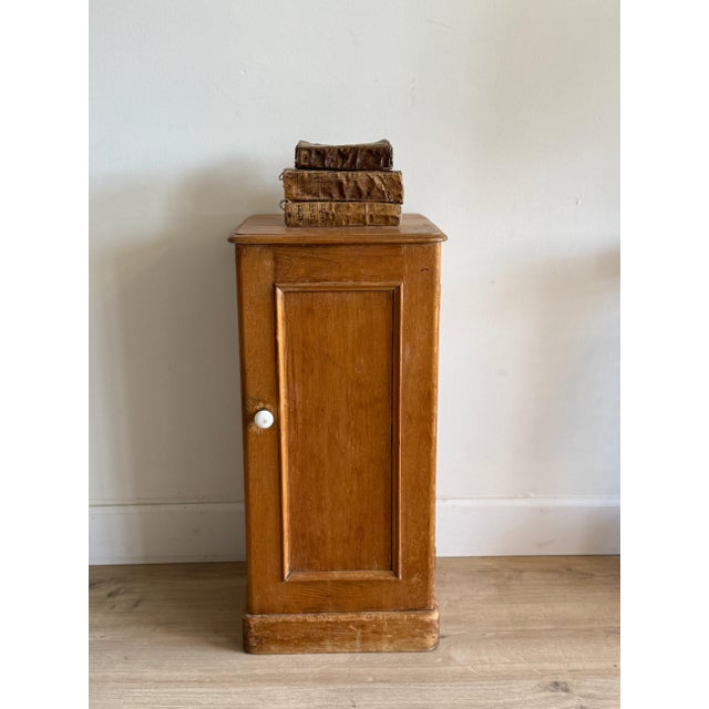 Honeyed English pine with a single paneled door and a small white porcelain knob. A low cabinet form with a recessed panel...