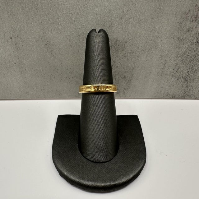 This designer Tiffany & Co. 1837 band ring is crafted in luxurious 18kt yellow gold and features the iconic Tiffany 1837...