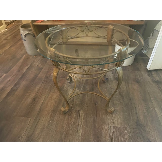An elegant round occasional table featuring an antiqued gold-tone metal base and a clear beveled-glass top. Open...