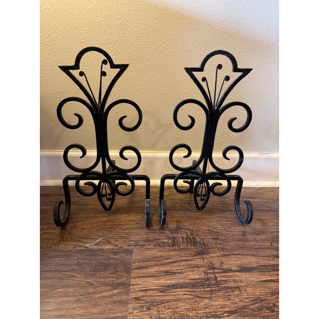 Elegant vintage wrought iron fireplace andirons featuring sculptural scrollwork and a stylized fleur-de-lis form. Hand-...
