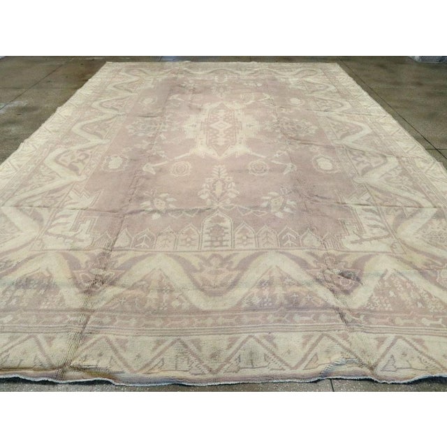 A vintage European Oushak large carpet. The light colors of this decorative Oushak belie the wild central cartouche...