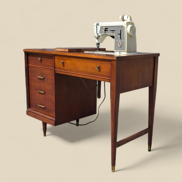 A Singer Slant-O-Matic 600 sewing machine housed in a streamlined mid-century wood cabinet. The machine folds beneath the...