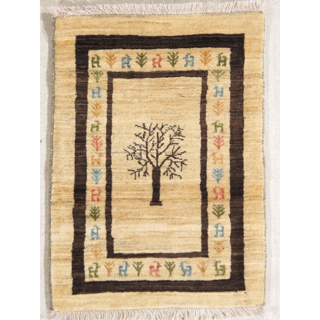 Hand-knotted Persian Gabbeh wool rug with a central tree motif on an ivory field, framed by dark brown borders and small...