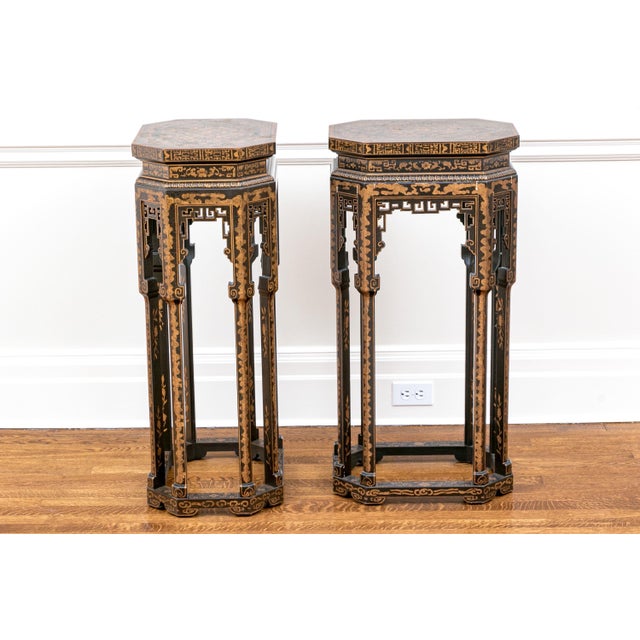 A pair of tall Chinese-style black lacquered pedestal stands with a gilt chinoiserie decoration and elongated octagonal...
