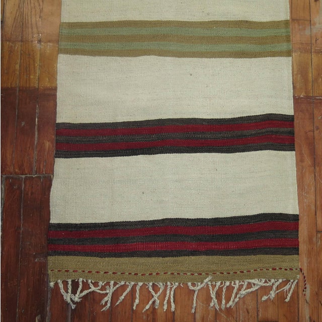 A mid-20th century narrow and long Turkish Kilim runner featuring an ivory colored ground, circa mid-20th century,...