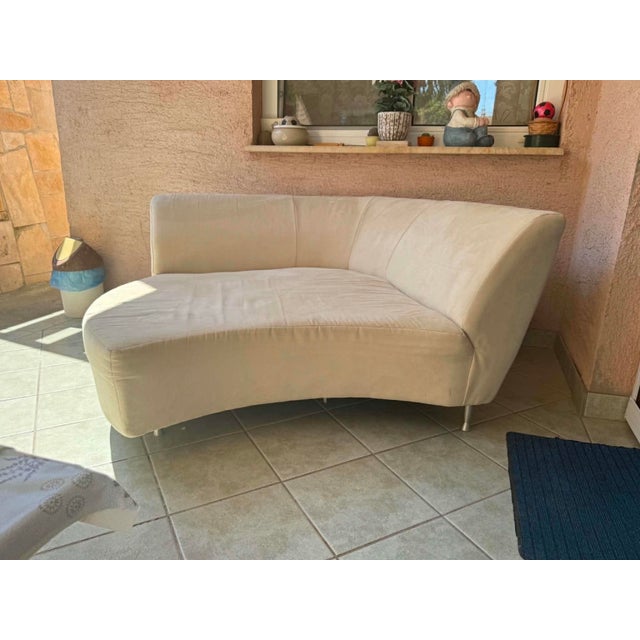 A sophisticated contemporary lounge sofa featuring an organic, curved silhouette. Upholstered in a soft cream-colored...