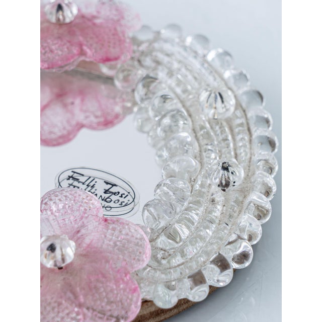This is a small oval Venetian wall mirror from Fratelli Tosi of Murano, with a handworked clear glass frame and two pink...