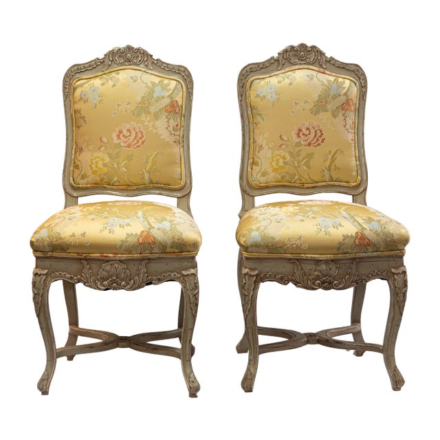 Pair of carved side chairs with floral yellow upholstery and detailed wood frames. Features shell and scroll motifs with...