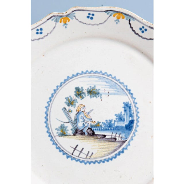 An 18th-century French faience plate from Nevers. It is decorated with a putto playing the violin under a tree, alongside...