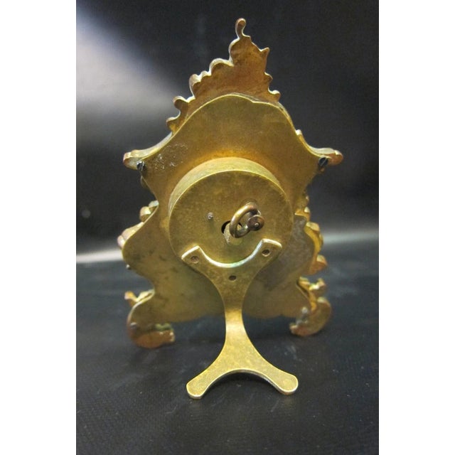 This fine vintage miniature clock in a decorative bronze frame features a detailed hand painted enamel scene of two women...