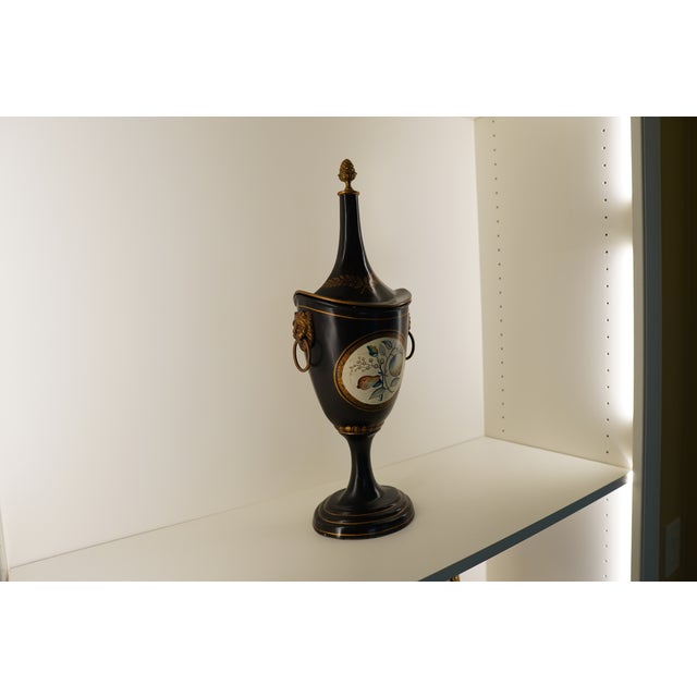 This tall black decorative piece features a pointed finial form with an urn-like center and subtle emblem detailing,...