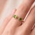 A bold, contemporary open-cuff ring featuring two vibrant green peridots — an oval-cut stone paired with a round-cut stone...
