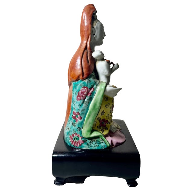 An 18th century Famille Rose figurine with a child sitting on a custom rosewood stand. The stand is from the 1920s to...