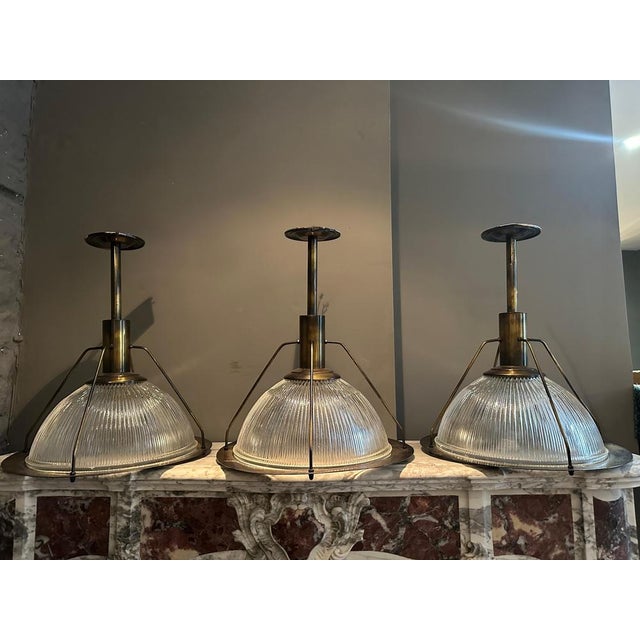 A set of three reclaimed Holophane style pendants. The ribbed dome glass shades withing a burnished and patinated brass...