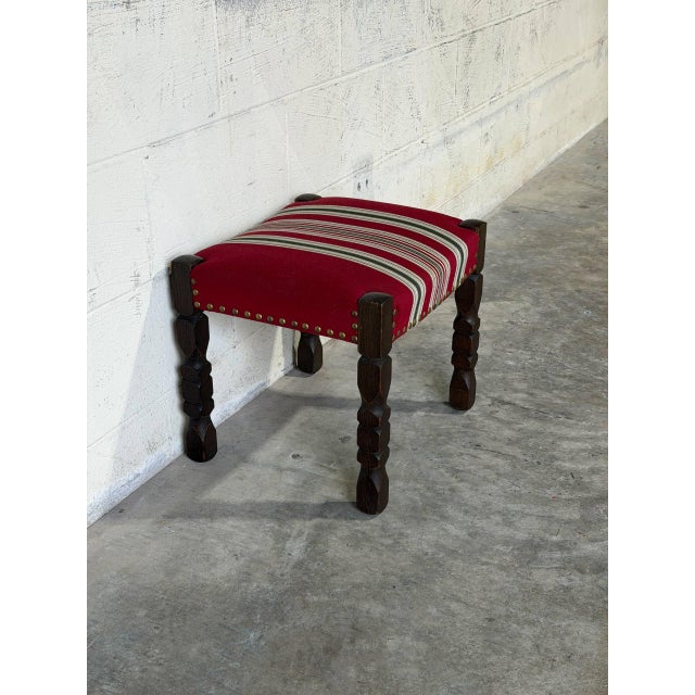 This classic footstool features a compact rectangular profile supported by intricately carved wooden spindle legs. The...