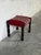 This classic footstool features a compact rectangular profile supported by intricately carved wooden spindle legs. The...
