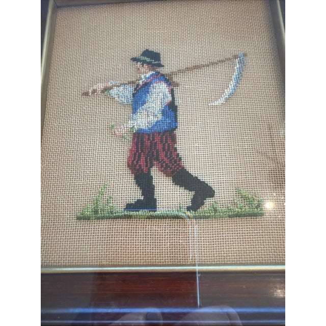 A charming vintage hand-stitched needlepoint depicting a folkloric peasant figure carrying a scythe, rendered in rich...