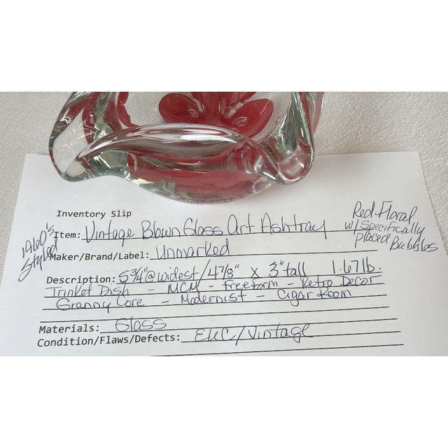 Vintage hand-blown glass art ashtray showcases a vibrant red floral design suspended within clear, heavy glass. The...