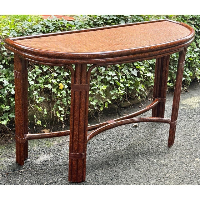 Vintage palm beach regency style console table. Lovely faux tortoise finish rattan, desirable demi lune shape, finished on...