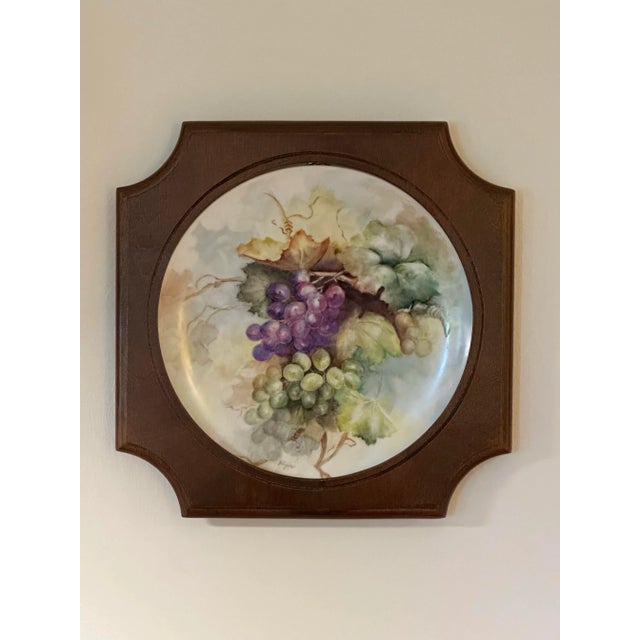 A unique shape on the solid wood frame borders this hand painted decorative plate. The still life, 10 inch wide plate is...