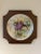 A unique shape on the solid wood frame borders this hand painted decorative plate. The still life, 10 inch wide plate is...